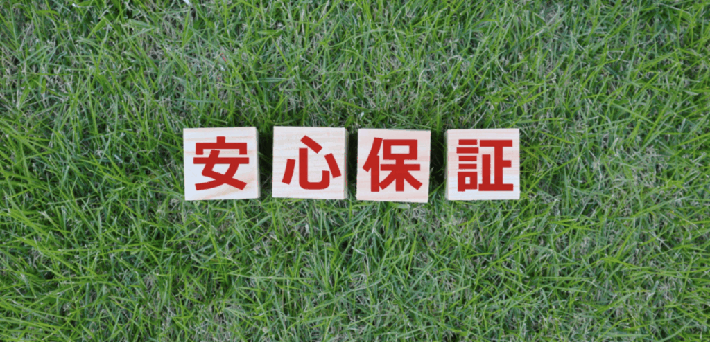 緑の芝生の上に木製ブロックを横一列に並べ、赤文字で「安心保証」と示した信頼・保証を訴求するビジュアル