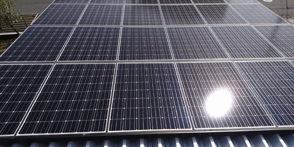 屋根一面に敷き詰められた太陽光パネルが強い日差しを受け、表面に光が反射して発電している様子