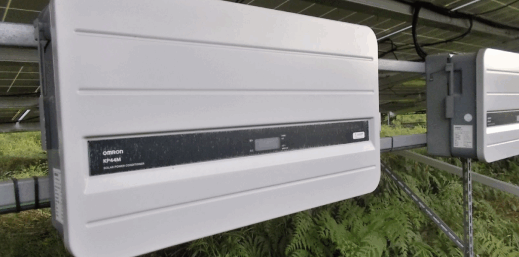 太陽光発電施設の架台に取り付けられた白い Omron KP44M パワーコンディショナーの接写